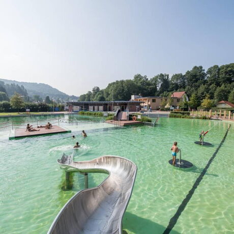 Aufnahme des Freibades BioBad Glücksbrunn mit Wasserrutsche, Wasserkanonen, und Liegeflächen